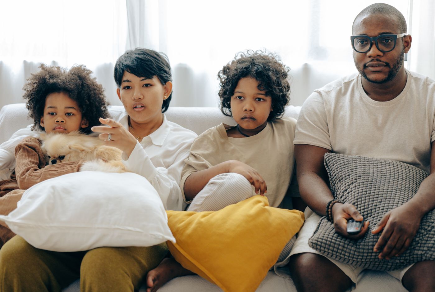A family sitting together on a sofa with a dog, watching something on the living-room TV