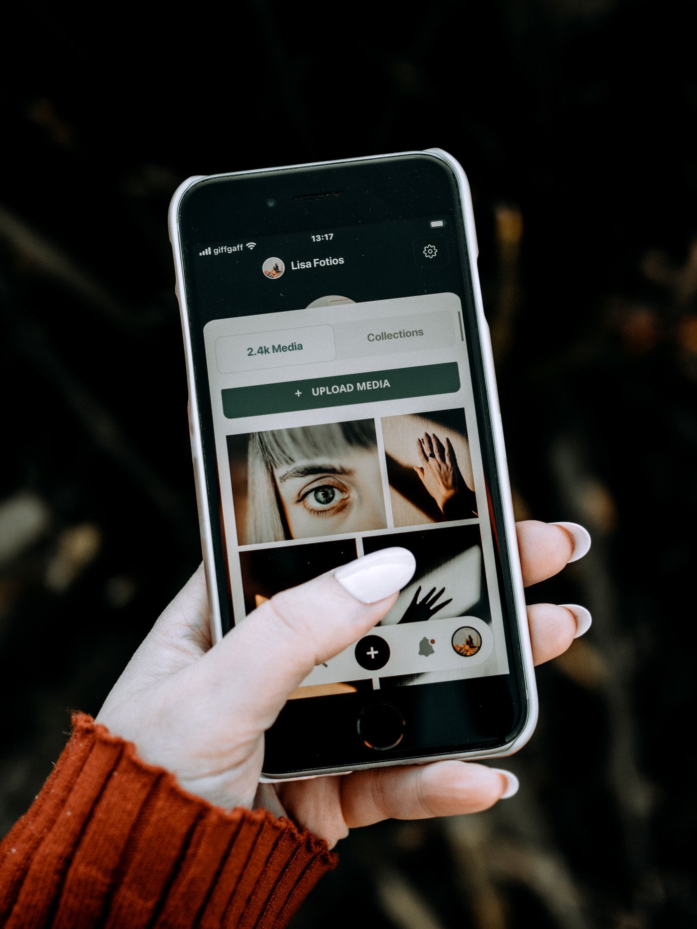 A hand holding a smartphone that shows a grid of photos and a media tab